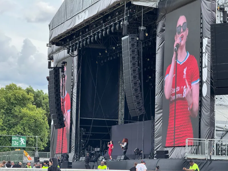 A prominent stage is set with a large screen showing a woman in a red shirt, actively addressing the audience.