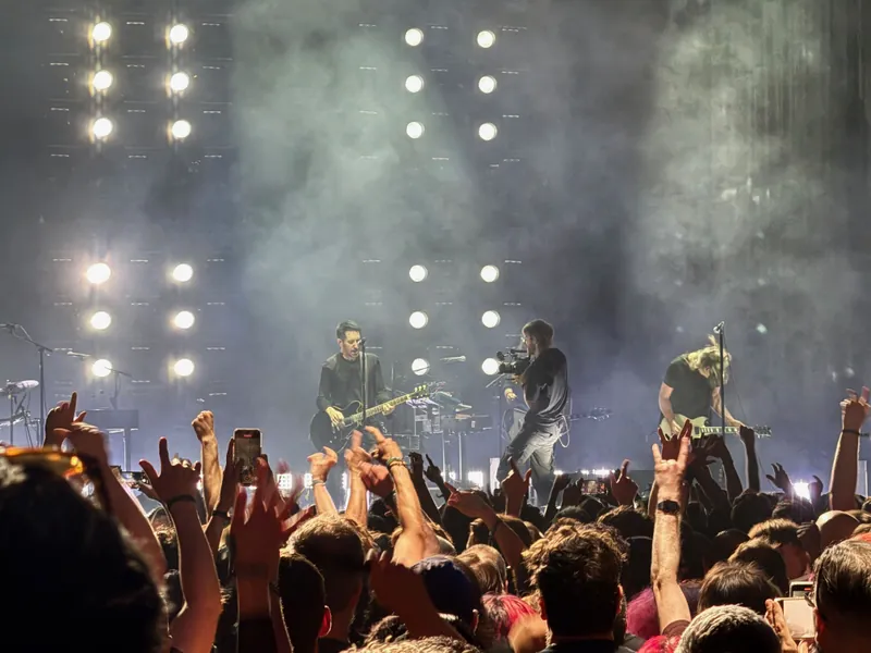 Trent playing guitar and the rest of the band around him. The crowd is light up with their hands in the air.