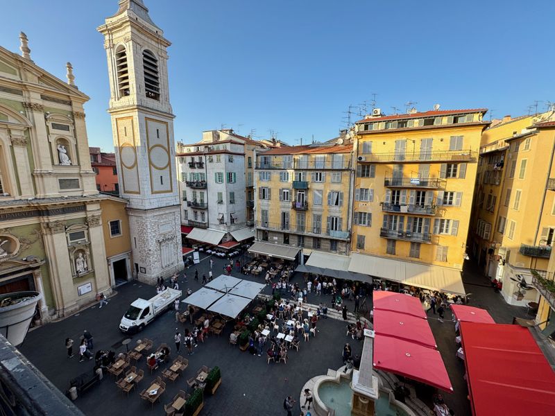 Wide angle image of an Italian looking plaza (that is in the south of France) with people milling around and eating at  restaurants and cafes