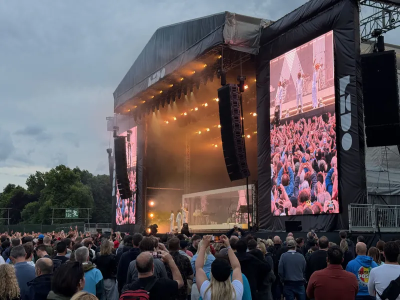 Large outdoor concert stage with a crowd of people and a large screen displaying a band performing.