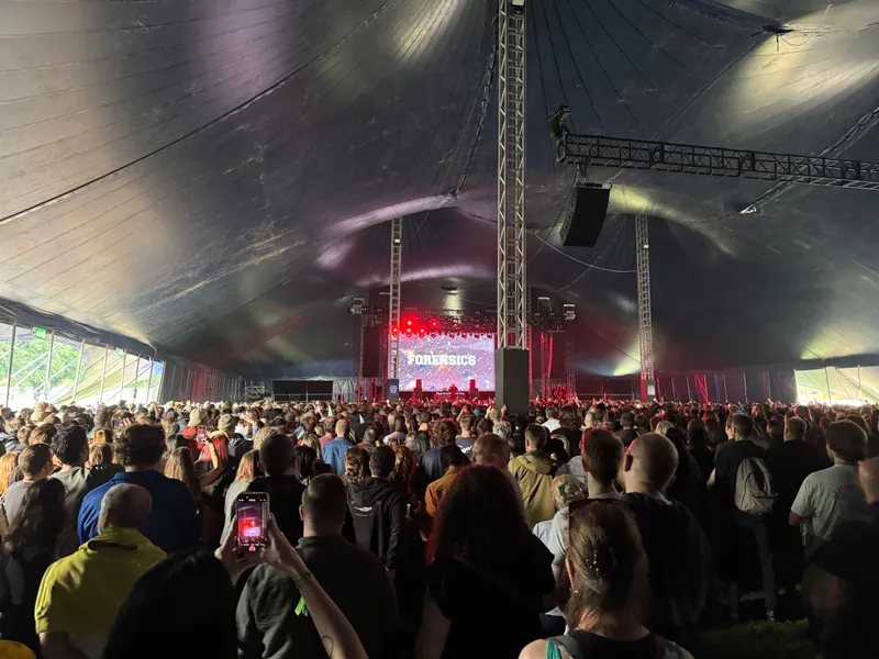 Large crowd packed inside a tent at a music festival, watching a band on stage.