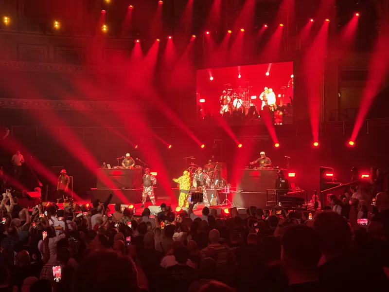 Flava Flav on stage. the sage is flooded in red light. there are two DJs on either side of the stage and a drummer in the middle.