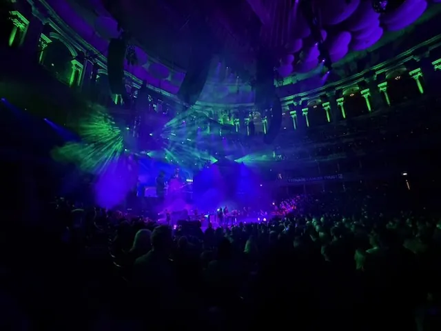 Wide-angle view of the Royal Albert Hall during Placebo's set, with vivid purple and green lighting sweeping across the stage and the hall's acoustic dishes visible on the ceiling above a packed crowd.