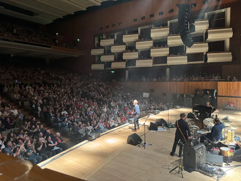 Wider shot of the entire auditorium. Glen is standing at the edge of the stage playing guitar.