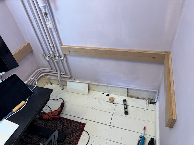 The corner of my office with tools lying on the floor and bare boards drilled into the wall