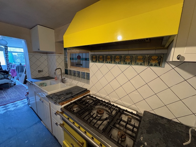 kitchen with yellow stove white tiles on the wall and white cabinets. There are still unfinished bits like no paint on the ceiling and no electrical sockets hooked up yet.
