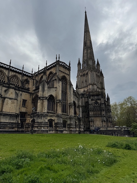 A wide angle shot of an old cathedral in Bristol with grey skies in the background and green grass in the foreground
