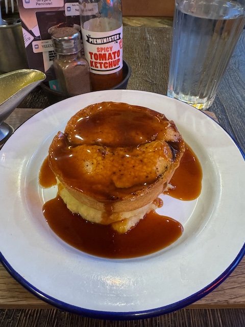 Classic British pie and mash on a white plate with gravy poured over it