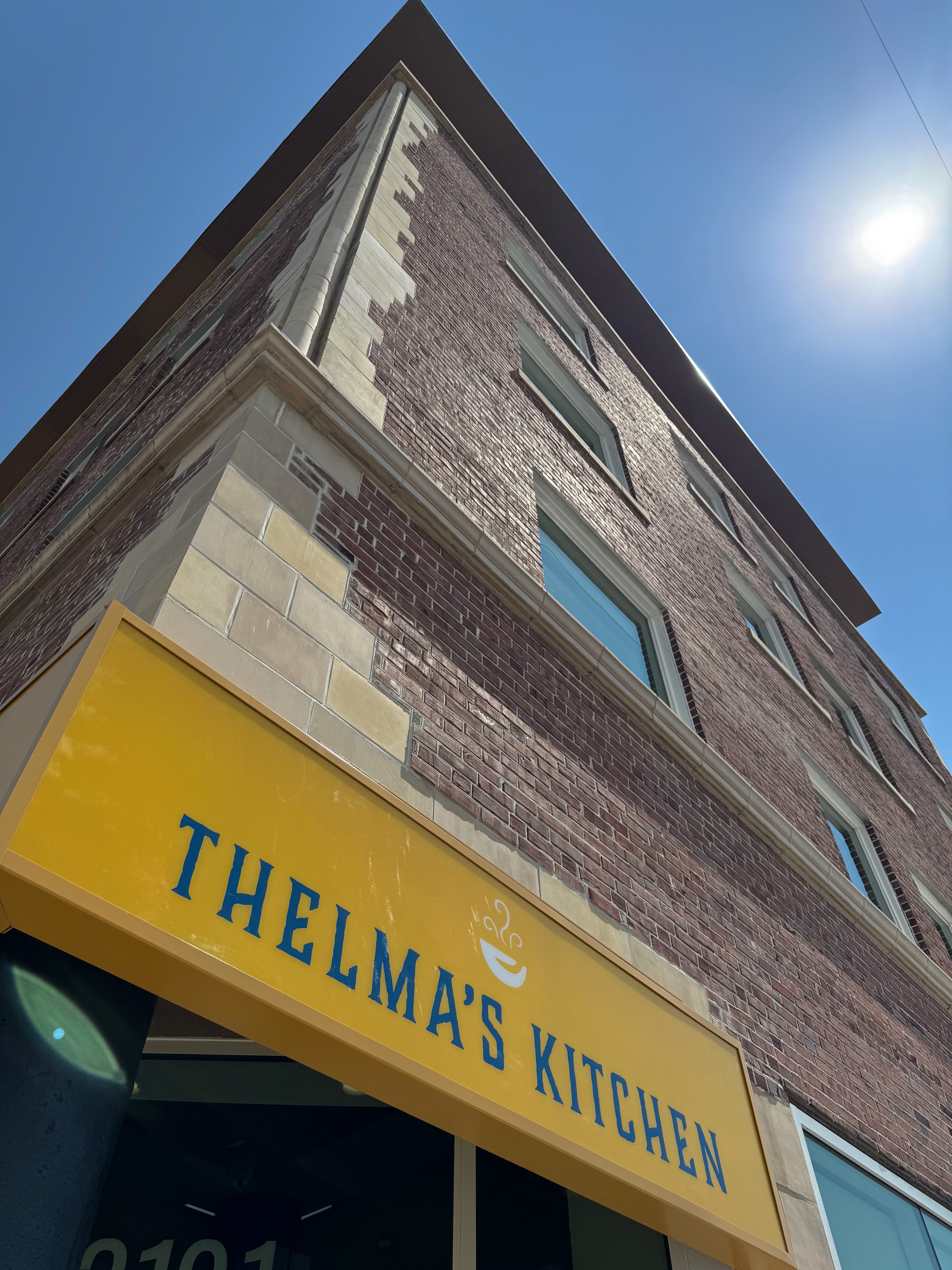 Looking up from the corner of the brick building. The sign for Thelma's Kitchen in the bottom.