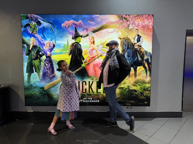 My daughter and I in pink accented outfits in front of the Wicked poster giving our best Galinda pose