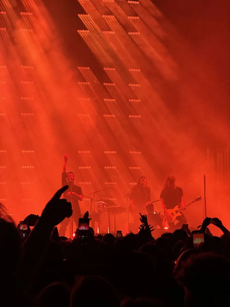 Red light blades flood the stage. People are raising their hands in front of the stage.