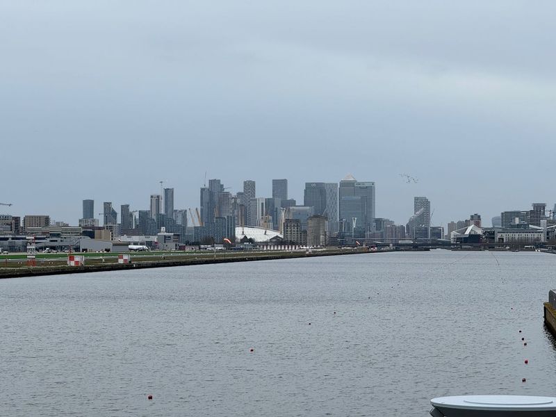 Docklands water in the foreground with London City Airport on the left and the buildings of Canary Warf in the distance