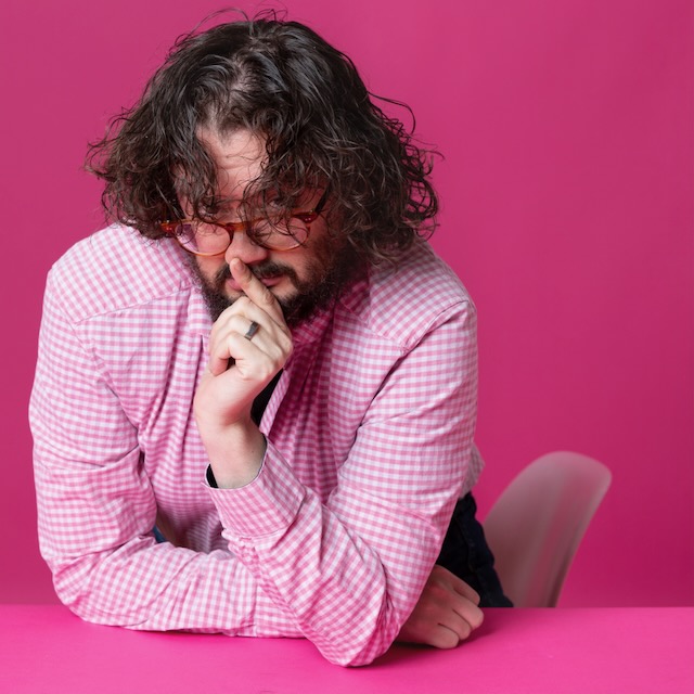 bit of a silly photo of myself posed with my hair in my face in front of a solid pink background