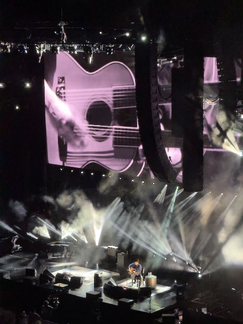 John sitting on a chair stage left  playing a double neck acoustic guitar