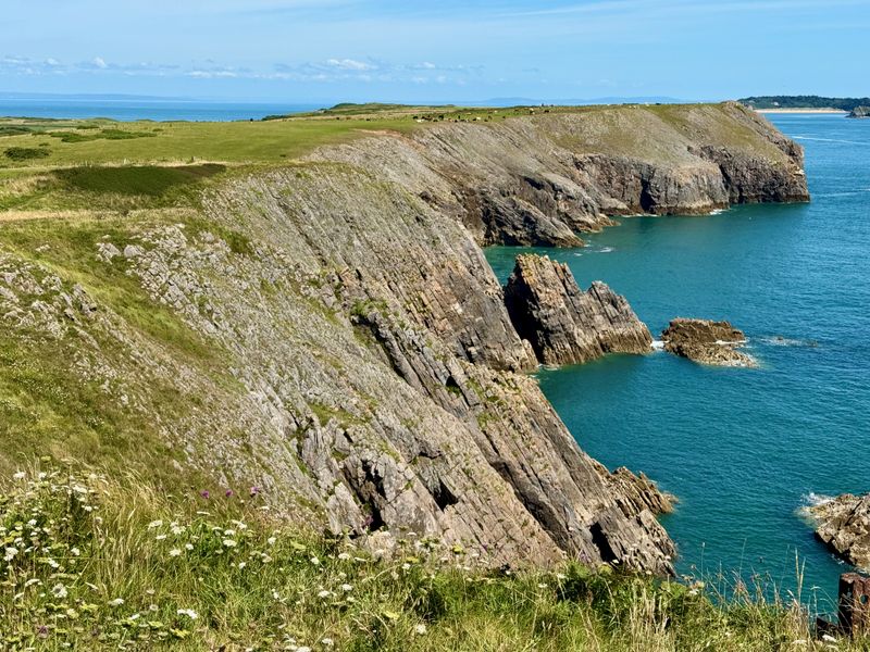 Sharp cliffs on the left with pastureland on top of them. They drop off very sharply into the sea.