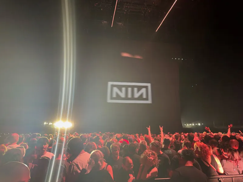 NIN logo projected on the stage with the crowd lit. The show has ended and people are milling around excitedly.