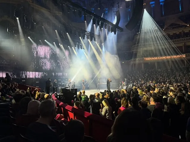 Wide shot of Garbage performing at the Royal Albert Hall, with dramatic white spotlights and a willow-like image projected on the screen. The packed auditorium and a "Teenage Cancer Trust" banner are visible.