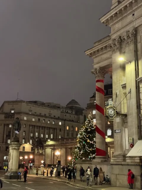 The columns of the Bank of England wrapped in large red ribbon looking like candy cane and a large Christmas tree out front all lit up.