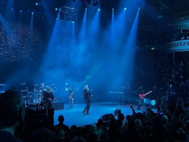 Garbage performing as a full band on the Royal Albert Hall stage bathed in blue light, with Shirley Manson at centre, guitarists on either side, and the ornate balconies of the venue visible in the background.
