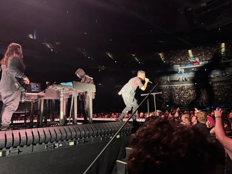 Trent Reznor leans out over the edge of the stage to sing to the crowd. Atticus Ross is behind him playing keyboards