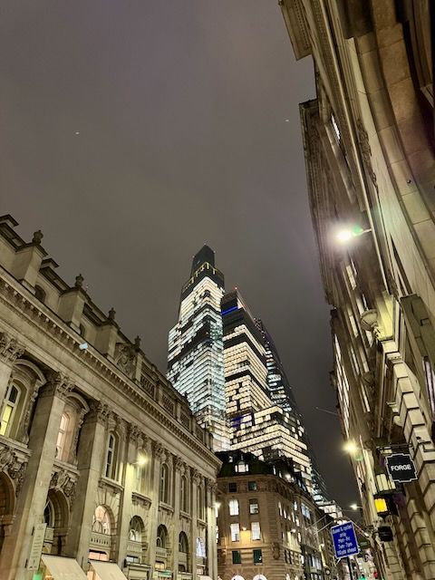 Night time, looking up at 22 Bishopsgate all lit up behind the smaller old stone buildings of London.